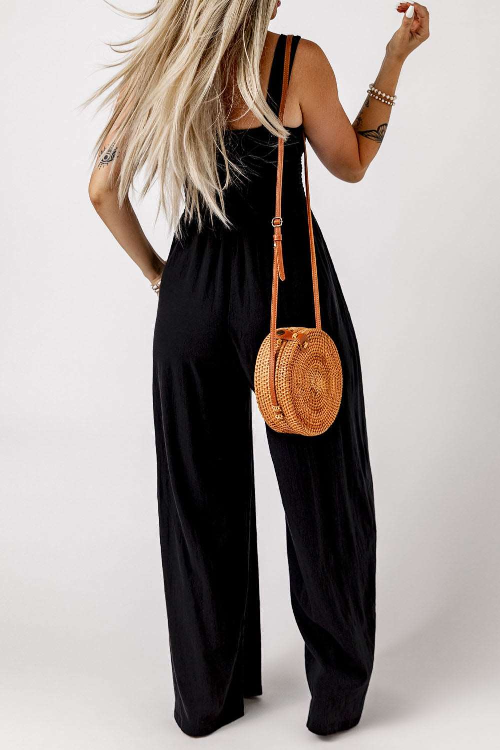 A woman in a black jumpsuit holding a purse, showcasing the Lots To Love Wide Leg Romper.